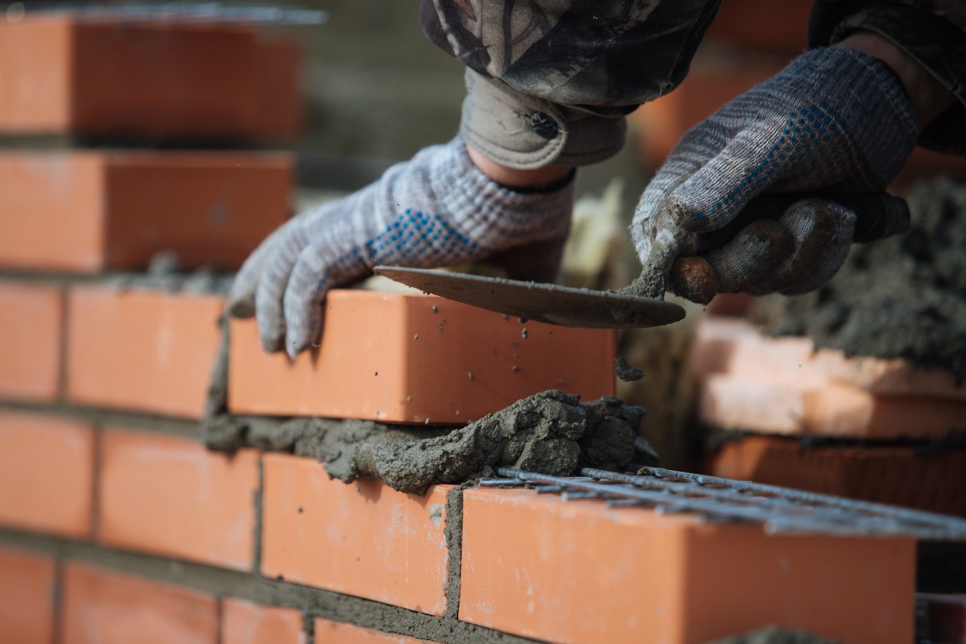 Mason laying brick with trowel and mortar on construction site