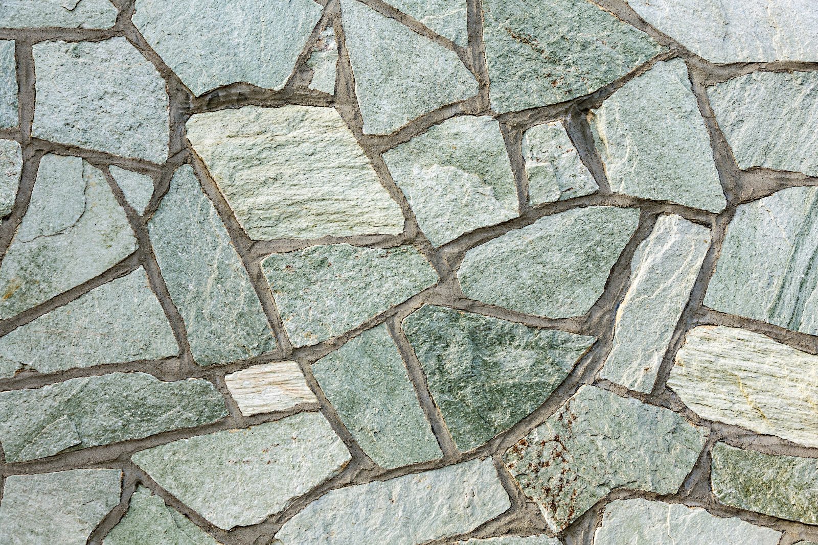 Close-up of irregular stone pavers in gray and green tones with mortar joints