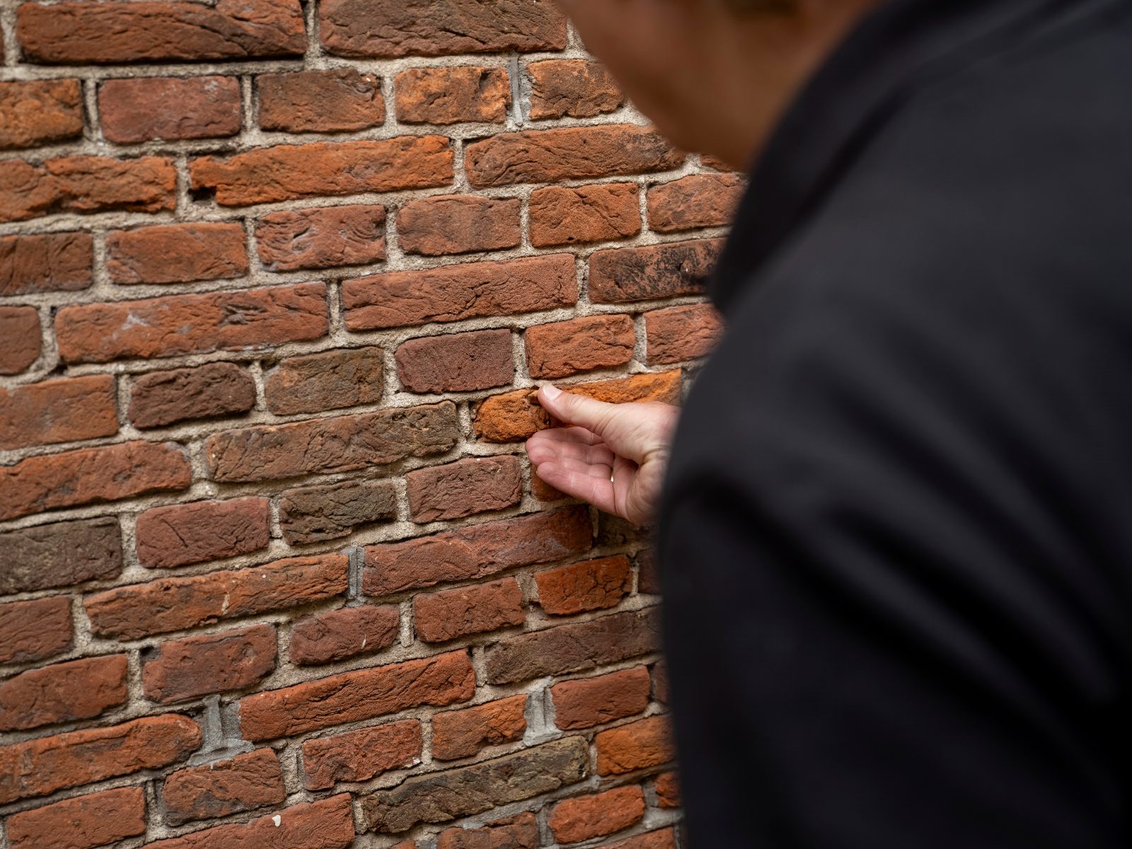 Person in dark clothing touching red brick wall with hand